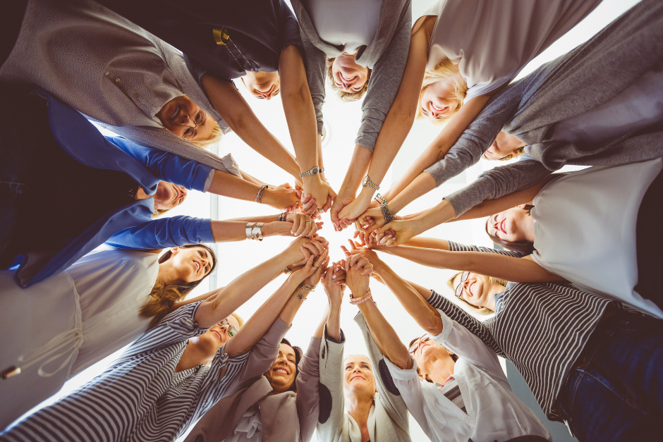 Group of women in a circle smiling and holding hands in the middle.